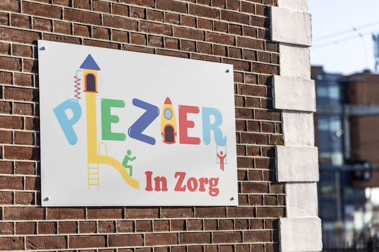 Logo van Plezier in Zorg op een bord gemonteerd op de zijkant van het gebouw.